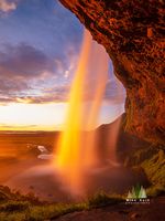 Seljalandsfoss Waterfall Sunset Glow, Iceland This captivating photograph captures the fiery golden light of sunset streaming through Seljalandsfoss waterfall in southern Iceland. Shot from behind the...