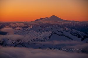 Over the North Cascades Mount Baker Sunset The last light of day paints Mount Baker and the surrounding North Cascades in glowing orange and violet tones as clouds drift among the peaks. Captured from...