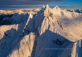 Over the North Cascades Pickets and Needles This breathtaking aerial photograph captures the razor-edged spires of the Pickets and the Needles in Washington’s North Cascades, glowing in the warm alpenglow...