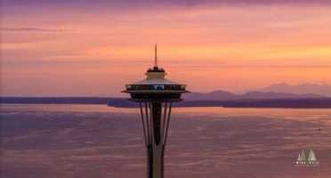 Aerial Seattle Sunset Space Needle Elliott Bay An aerial sunset view of Seattle’s Space Needle overlooking Puget Sound and the distant Olympic Mountains. The sky glows in warm tones of orange, pink, and...