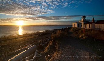 Discovery Park Lighthouse Sunset Evening The last light of day sweeps across Puget Sound as the sun dips low beside Discovery Park Lighthouse. Golden rays reflect off the water and driftwood-strewn...