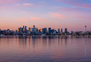 Seattle Skyline Photography Sunrise Seattle skyline at sunrise reflected in Lake Union with the Space Needle and downtown buildings glowing in warm morning light under pastel pink clouds.