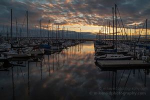 Shilshole Marina Calm Sunset Clouds Sunset over Shilshole Bay Marina in Seattle with rows of sailboats reflected in still water beneath glowing clouds and warm evening light.