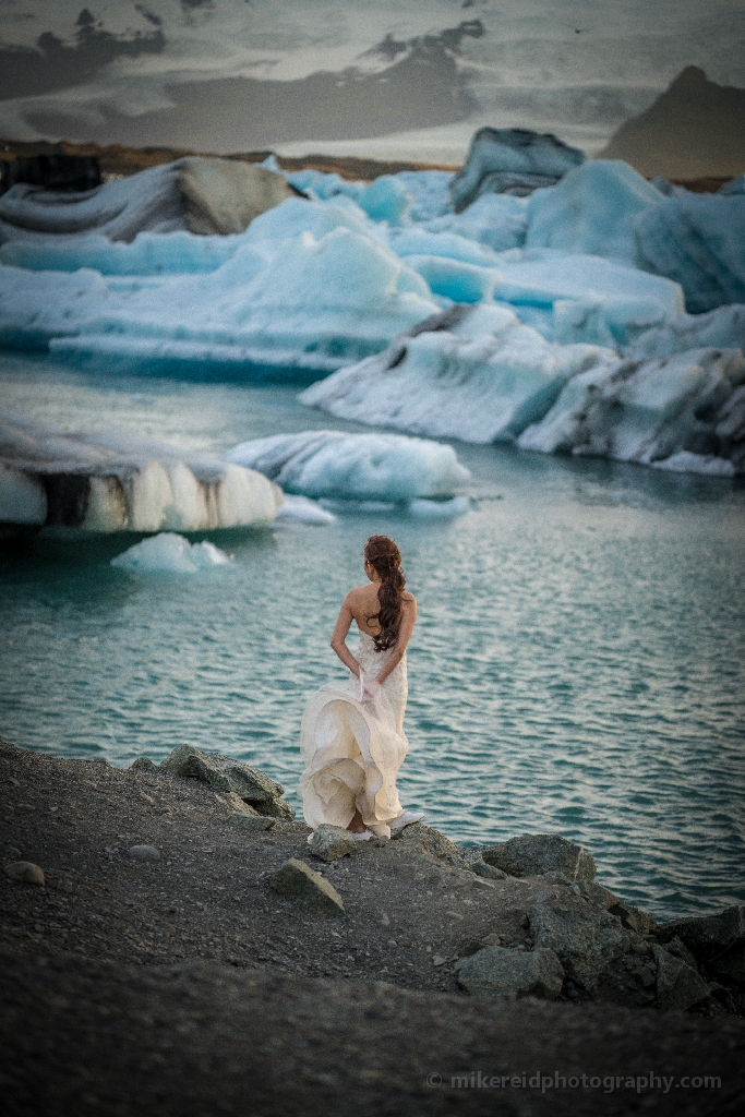 Iceland Jokulsarlon Bride Photography A serene moment unfolds as a figure stands before the blue icebergs of Jökulsárlón Glacier Lagoon, surrounded by glacial light and Arctic stillness. The soft tones and textures create a surreal, almost painterly atmosphere that captures Iceland’s haunting beauty and sense of solitude. Fine-art photograph by Mike Reid blending elegance, emotion, and landscape.