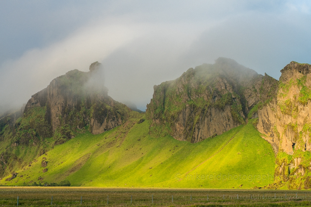 South Iceland Lush Cliffs – Ring Road Landscape with Misty Light | Fine Art Photography Soft morning mist drifts across the vibrant green cliffs of South Iceland along the Ring Road. Sunlight filters through the fog, revealing the rich textures and volcanic contours of this dramatic landscape. Captured by Mike Reid Photography, this fine art image showcases the lush, otherworldly beauty that defines Iceland’s southern coast.