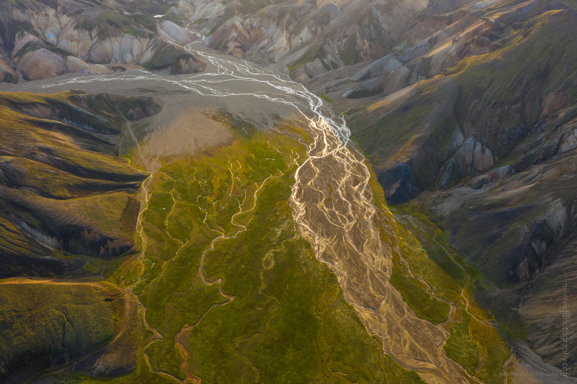 Sunlit Vondugil Valley – Aerial View of Landmannalaugar Highlands Iceland Golden sunlight illuminates Vondugil Valley in the Icelandic Highlands, revealing a mesmerizing tapestry of braided rivers, mossy slopes, and volcanic ridges. Captured from above, this fine art aerial photograph showcases the dynamic beauty of Landmannalaugar — where light, color, and texture merge to define Iceland’s most painterly landscape. A celebration of nature’s design in one of Iceland’s most remote regions.