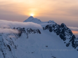 Over the North Cascades Backside of Shuksan Sunset This aerial photograph captures the dramatic north and east faces of Mount Shuksan, veiled in drifting clouds as the first light of sunrise crests its icy...