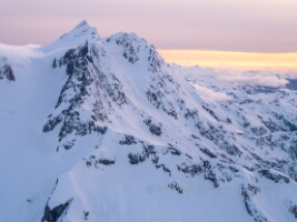 Over the North Cascades North Face of Shuksan A sweeping aerial view of Mount Shuksan’s dramatic north face, where steep snowfields and dark volcanic rock carve striking patterns beneath a pastel dawn sky....