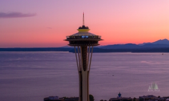 Aerial Seattle Space Needle Sunset Layers The Seattle Space Needle glows at sunset against a vivid pink and purple sky over Puget Sound. The calm evening light reflects on the water and distant Olympic...