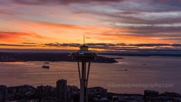 Aerial Seattle Space Needle Sunset Light Aerial view of Seattle’s Space Needle at sunset with ferries crossing Elliott Bay and West Seattle beyond. The sky burns with orange and magenta streaks as the...