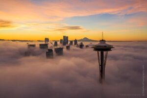 Over Seattle Space Needle Above the Fog A breathtaking sunrise over Seattle as the Space Needle rises above a sea of fog, with the downtown skyline and Mount Rainier glowing softly in the morning...