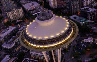 Seattle Aerial Dusk Space Needle Aerial night view of Seattle’s Space Needle illuminated against the city lights below. The glowing observation deck and soft streetlights create a striking...