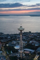 Seattle Aerial Photography Above the Space Needle at Dusk Aerial sunset over the Space Needle and Seattle waterfront, glowing golden above Puget Sound with the Olympic Mountains in the distance.
