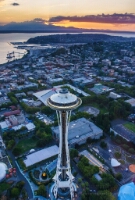 Space Needle Sunset Closeup Aerial sunset over the Space Needle and Seattle waterfront, glowing golden above Puget Sound with the Olympic Mountains in the distance.