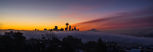 Seattle in the Fog at Sunrise A breathtaking panoramic view of Seattle at sunrise, as a soft layer of fog drifts gracefully across the city skyline. The Space Needle and downtown high-rises...