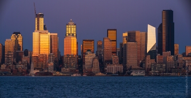 Seattle Photography City Sunset Reflection from Alki Details Seattle skyline at sunrise with golden reflections on downtown skyscrapers, including the Columbia Center and the F5 Tower, glowing above Elliott Bay under...