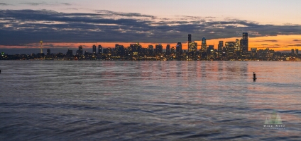Seattle Sunset Elliott Bay Seattle skyline at sunset from Alki Beach, with the Space Needle and downtown buildings glowing under dramatic clouds and soft reflections on the calm waters of...