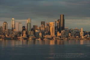 Warm Seattle Sunset Skyline Across Elliott Bay from Alki Golden evening light washes over the Seattle skyline as seen from Alki Beach, reflecting warmly across the calm waters of Elliott Bay. Iconic towers — from the...
