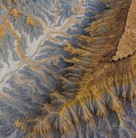 Erosion Patterns Below a Utah Mesa — Aerial Desert Landscape An aerial view of a Utah mesa reveals a mesmerizing landscape sculpted by wind and water. The ridges and canyons flow outward in organic patterns of gold, slate...