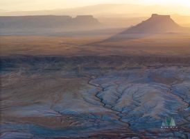 Sunset Over Factory Mesa, Utah — Aerial Desert Landscape An aerial view of Factory Mesa, Utah, bathed in the warm glow of sunset light. The scene unfolds in layers of golden desert, blue clay canyons, and rugged...