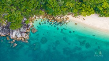 Aerial View of Nudey Beach, Fitzroy Island – Turquoise Coral Waters and Tropical Coast An exquisite aerial photograph of Nudey Beach on Fitzroy Island near Cairns, Queensland. The image captures the vivid contrast of emerald rainforest, smooth...