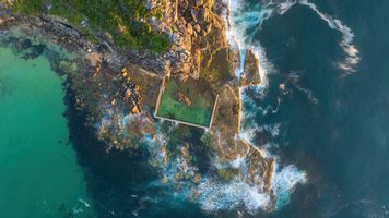 Sunrise Aerial Over Curl Curl Ocean Pool – Sydney Northern Beaches Coastline A breathtaking aerial view of Curl Curl Ocean Pool at sunrise, where golden light illuminates the rock platform and waves crash against the rugged coastline of...