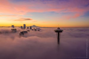 Over Seattle City and Space Needle at Sunrise Above the Clouds A beautiful sunrise over Seattle as the Space Needle rises above a sea of fog, with the downtown skyline and Mount Rainier glowing softly in the morning light....