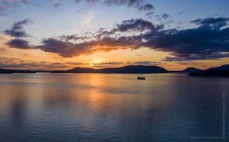 Over San Juan Islands Ferry Sunset Aerial Photography A Washington State ferry glides across the Salish Sea as the sun sets behind the San Juan Islands, painting the sky in warm orange and violet hues. The tranquil...