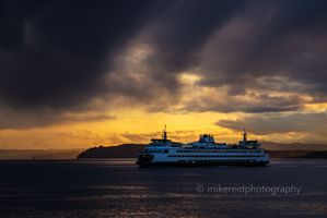 Seattle Photography Stormy Sunset Ferry Ride Washington State Ferry crossing Elliott Bay at sunset beneath dramatic storm clouds and golden light over the Puget Sound.