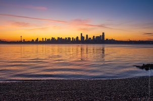 Seattle Waterfront Sunrise Kayaker Tranquil sunrise over the Seattle skyline from Alki Beach with golden light reflecting across Elliott Bay and the Space Needle silhouetted against the horizon....