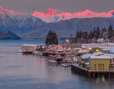 Devil’s Thumb Alpenglow Over Petersburg Alaska Brilliant pink alpenglow illuminates Devil’s Thumb and the surrounding snow-covered Coast Mountains above the waterfront in Petersburg, Alaska. Below, snowy...