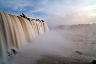 Iguazu Falls in Misty Morning Light A close view of Iguazu Falls with a broad curtain of water plunging into dense mist below. Soft light filters through the spray, while distant waterfalls fade...