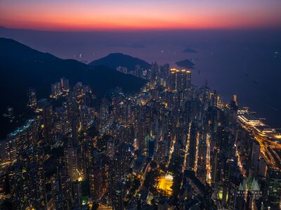Hong Kong Coastal Skyline and City Lights at Twilight A sweeping aerial view of Hong Kong's densely packed coastal skyline at twilight, as thousands of city lights glow beneath a brilliant pink and violet evening...