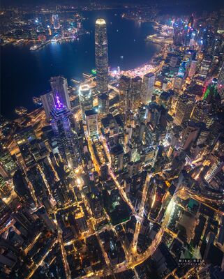 Hong Kong Financial District at Night Vertical Aerial Panorama A dramatic vertical drone panorama looks down over Hong Kong's Central financial district at night. Illuminated skyscrapers rise above a dense network of...