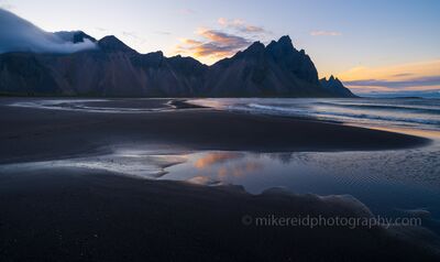 Stokksnes Sunset Reflections – Iceland Black Sand Beach Soft evening light glows across the black sands and tidal pools of Stokksnes, with the jagged Vestrahorn Mountains rising in the distance. Captured by Mike Reid...