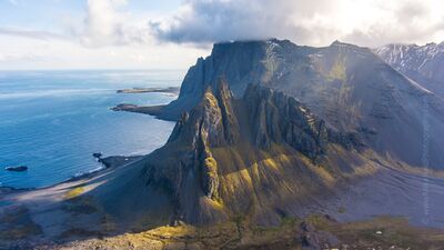 Over Iceland Drone Vestrahorn Dusk A breathtaking aerial photograph of Vestrahorn Mountain along Iceland’s southeast coast, where sharp volcanic ridges rise dramatically above black sand beaches...