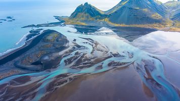 Over Iceland Drone Vestrahorn Winding Blue Rivers An ethereal aerial photograph over the Stokksnes estuary in southeastern Iceland, where glacial meltwater fans into the sea beneath the dramatic peaks of...