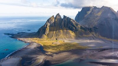 Vestrahorn Aerial View – Iceland’s Iconic Coastal Peaks A breathtaking aerial photograph of Vestrahorn Mountain along Iceland’s southeast coast, where sharp volcanic ridges rise dramatically above black sand beaches...