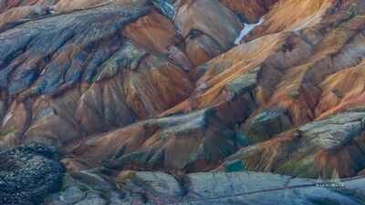 Layered Rhyolite Ridges of Landmannalaugar An aerial view across the layered rhyolite mountains of Landmannalaugar in Iceland’s Highlands. Warm rust and gold slopes fold through blue-gray volcanic...