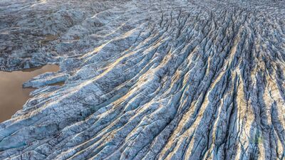 Hoffellsjökull Glacier Ice Patterns Aerial, Iceland Golden morning light traces the intricate ridges and deep blue crevasses of Hoffellsjökull Glacier in southeastern Iceland. Photographed from above, the immense...