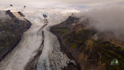 Glacial Road, Iceland – Aerial View of Flowing Ice and Mountain Valleys This dramatic aerial photograph captures a glacier carving its path through Iceland’s rugged mountain landscape, creating what appears to be a natural “road” of...
