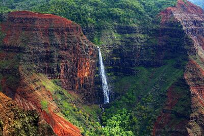 Waimea Canyon Waterfall Among Red Cliffs Kauai Hawaii A slender waterfall plunges down the rugged volcanic cliffs of Waimea Canyon on the Hawaiian island of Kauai. Rich red and rust-colored rock formations contrast...