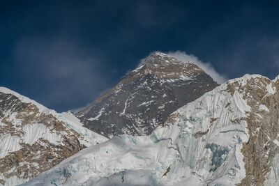 Mount Everest Emerging Above the Glaciers of Nuptse The dark pyramidal summit of Mount Everest emerges between the immense snow-covered ridges of Nuptse in Nepal's Khumbu region. Photographed with a telephoto...