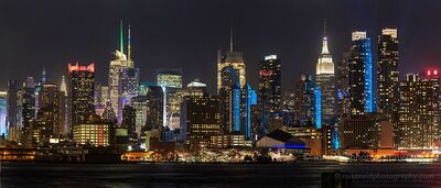 Midtown Manhattan Skyline with Blue Lights at Night from New Jersey The illuminated Midtown Manhattan skyline glows across the Hudson River, photographed at night from the New Jersey waterfront. The Empire State Building rises...