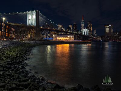 Brooklyn Bridge and DUMBO Waterfront at Night New York City The illuminated Brooklyn Bridge stretches across the East River at night, with the skyscrapers of Lower Manhattan and One World Trade Center rising beyond its...