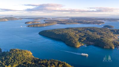Aerial Ferry Passing Shaw Island in the San Juan Islands A Washington State Ferry curves past Shaw Island through the blue waterways of the San Juan Islands. From above, the ferry wake traces a clean path between...