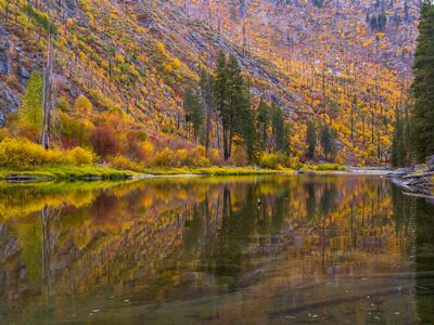 Autumn Reflections Beneath Tumwater Canyon A broad, calm stretch of water reflects the steep autumn-covered slopes of Tumwater Canyon near Leavenworth, Washington. Gold, orange, and red foliage spreads...