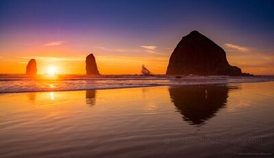 Golden Sunset Reflections at Haystack Rock Golden sunset light reflects across the wet sand at Cannon Beach as Haystack Rock and the Needles rise in silhouette from the Pacific. Warm orange light, gentle...