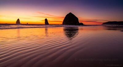 Haystack Rock and Tidal Sand at Sunset Low tide reveals rippled sand and shallow reflections at Cannon Beach as Haystack Rock and the Needles stand in silhouette against a glowing Oregon Coast...