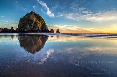 Haystack Rock in Golden Evening Light, Cannon Beach Warm evening light touches Haystack Rock at Cannon Beach, Oregon, while its reflection stretches across the wet sand at low tide. The cool blue sky and soft...